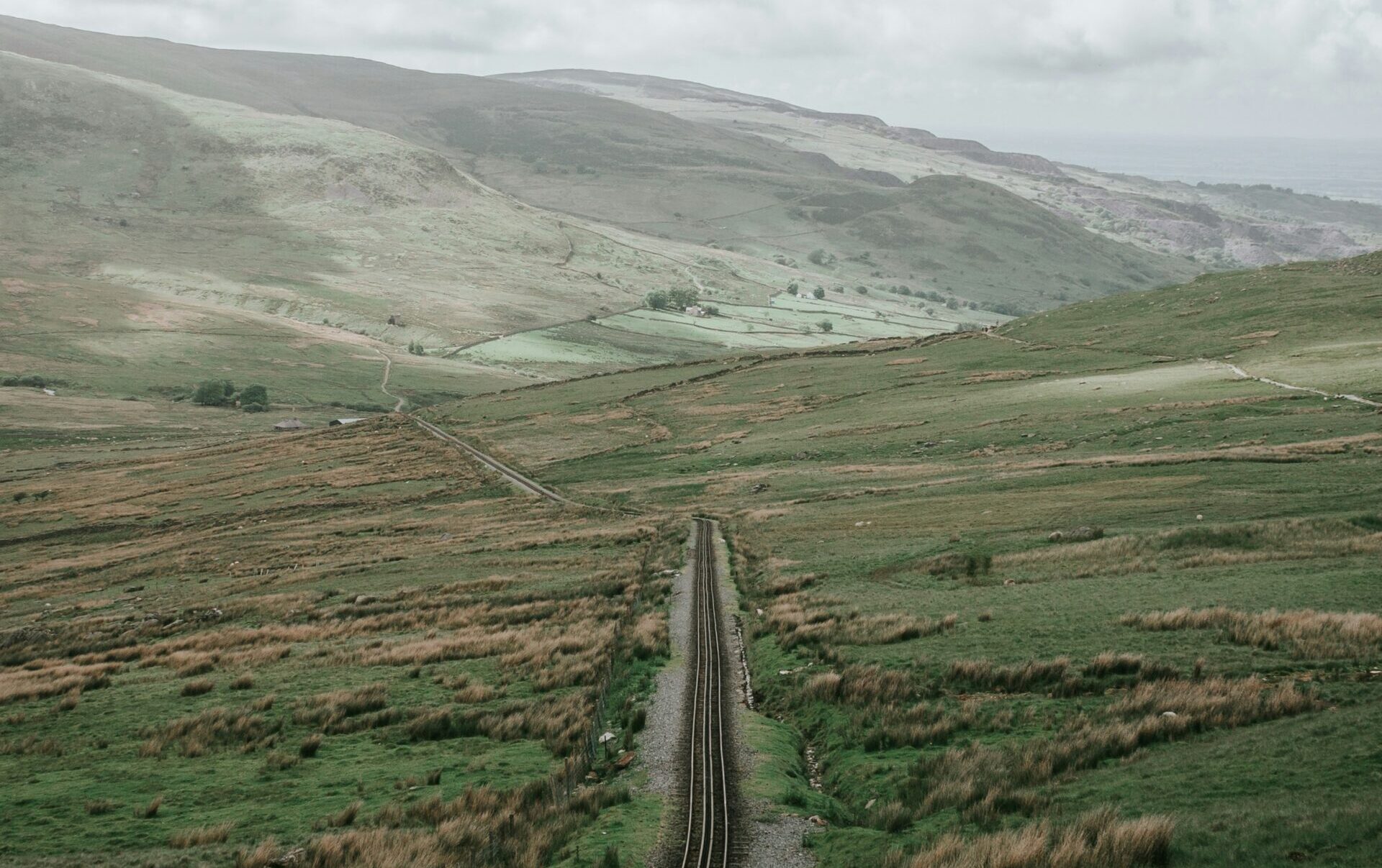 A picture of a road cutting through a mountain, leading towards a cloudy horizon.