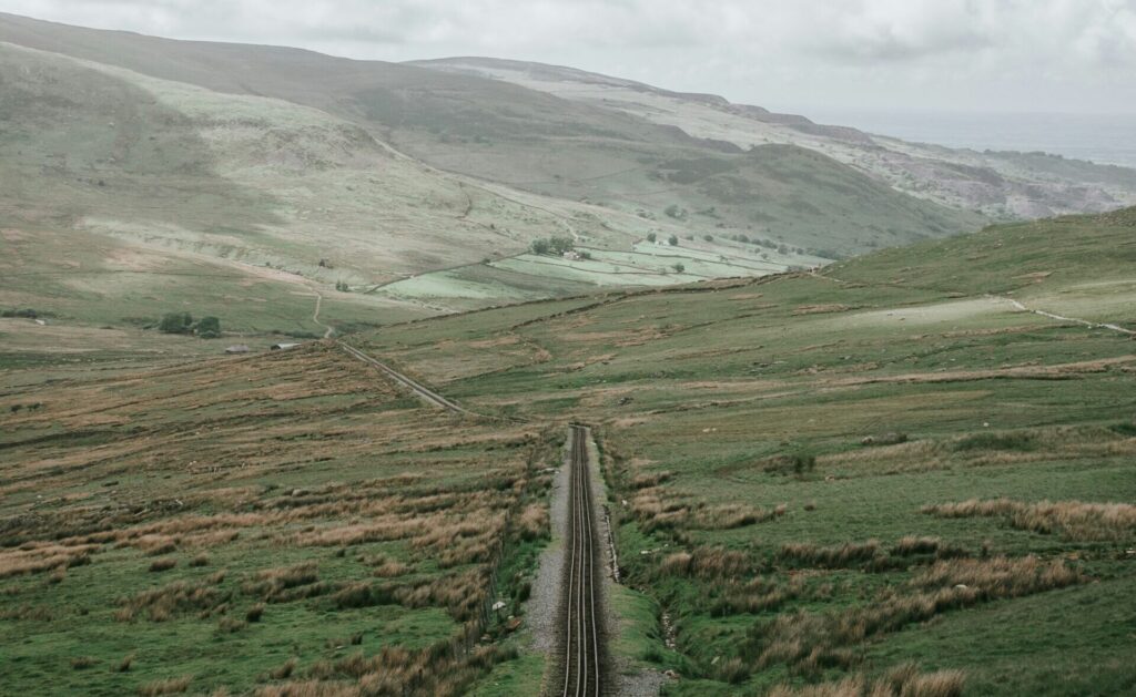 A picture of a road cutting through a mountain, leading towards a cloudy horizon.