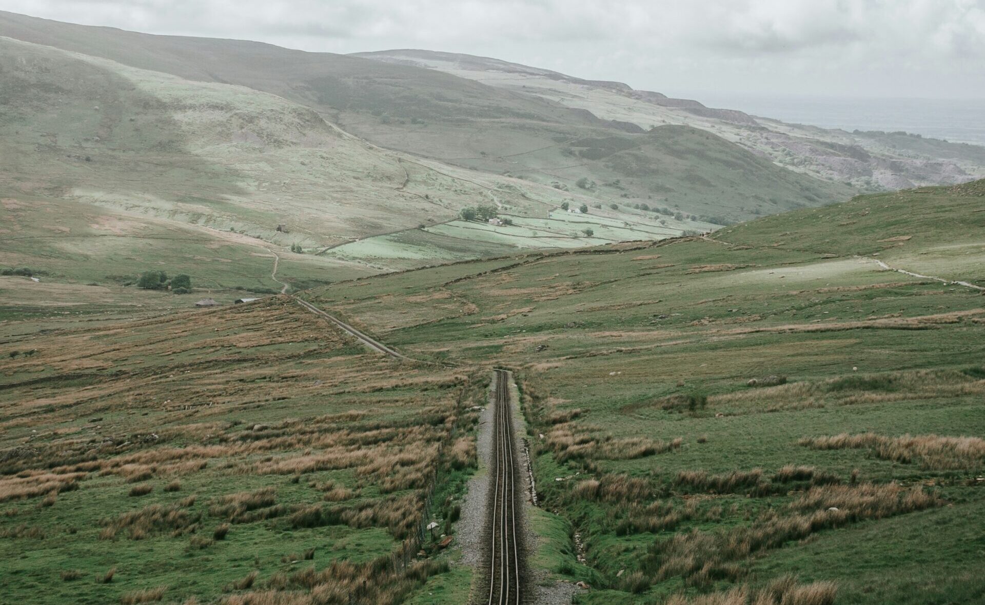 A picture of a road cutting through a mountain, leading towards a cloudy horizon.