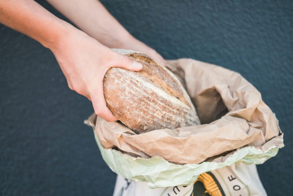 Two hands holding a loaf of bread coming out of a flour bag.